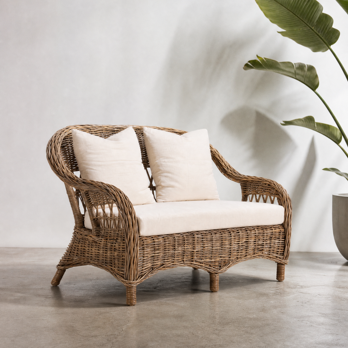 A two-seater Monterrey sofa made of rattan in a natural gray finish, with white fabric cushions.