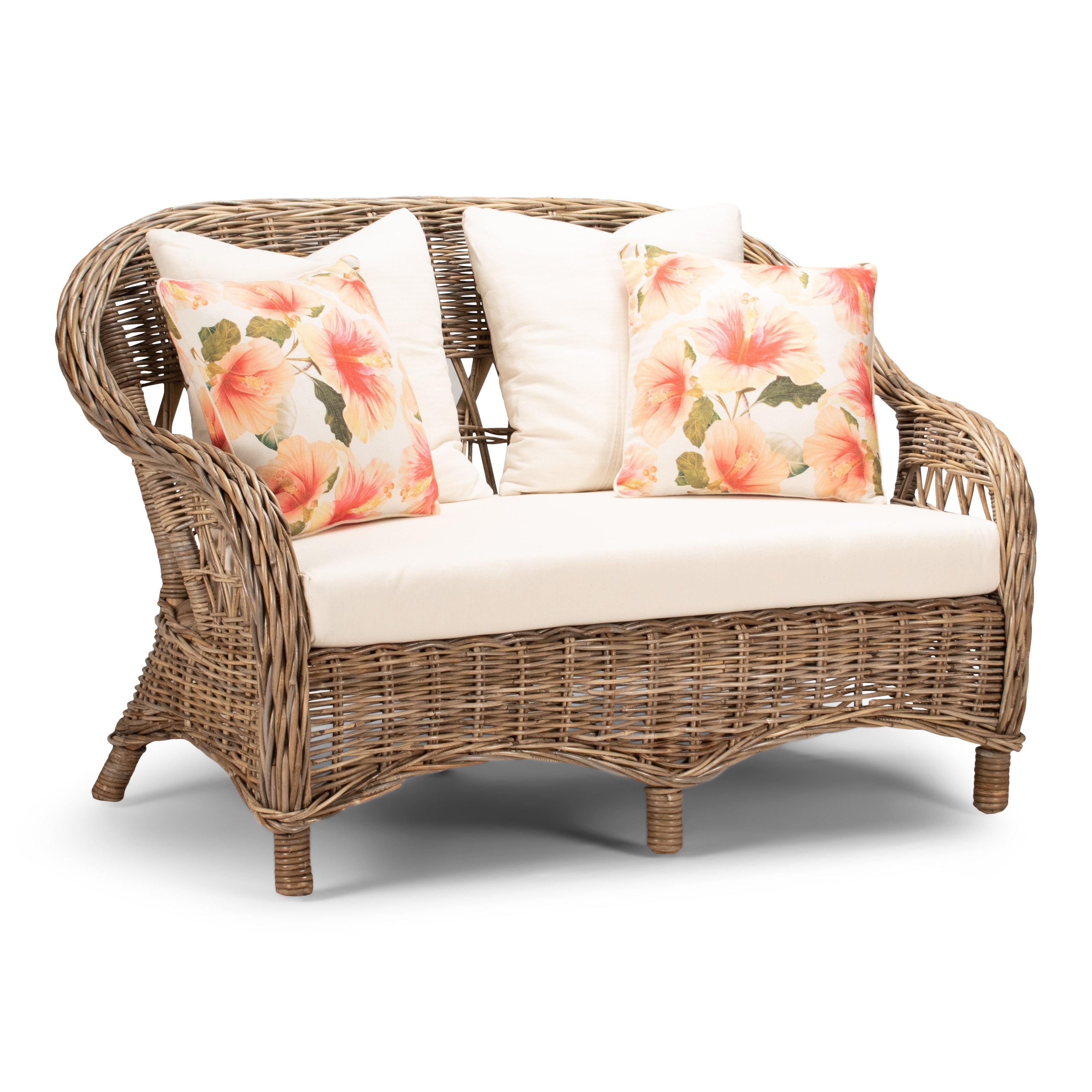 A two-seater Monterrey sofa made of rattan in a natural gray finish, with white fabric cushions and two pillows with a floral design.